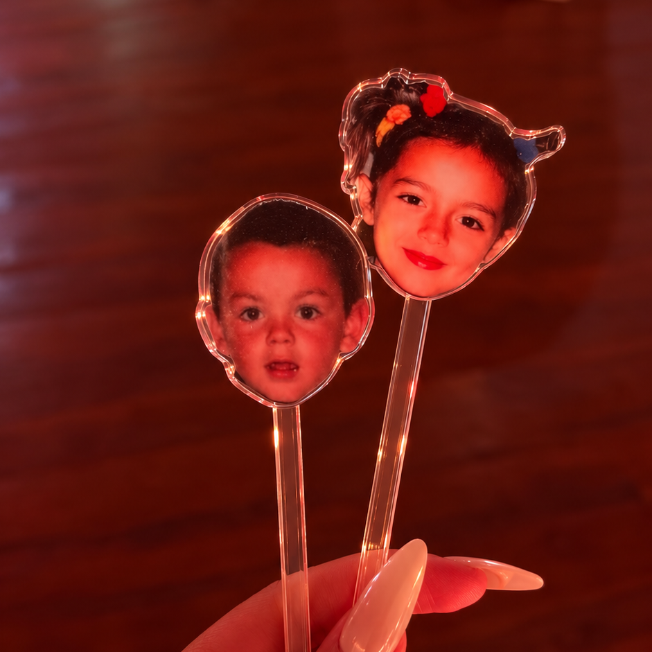 Two clear drinks stirrers with personalised childhood photo face designs