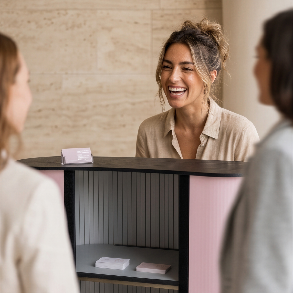 A woman is smiling and laughing while standing behind a counter, with two other people visible in the foreground.