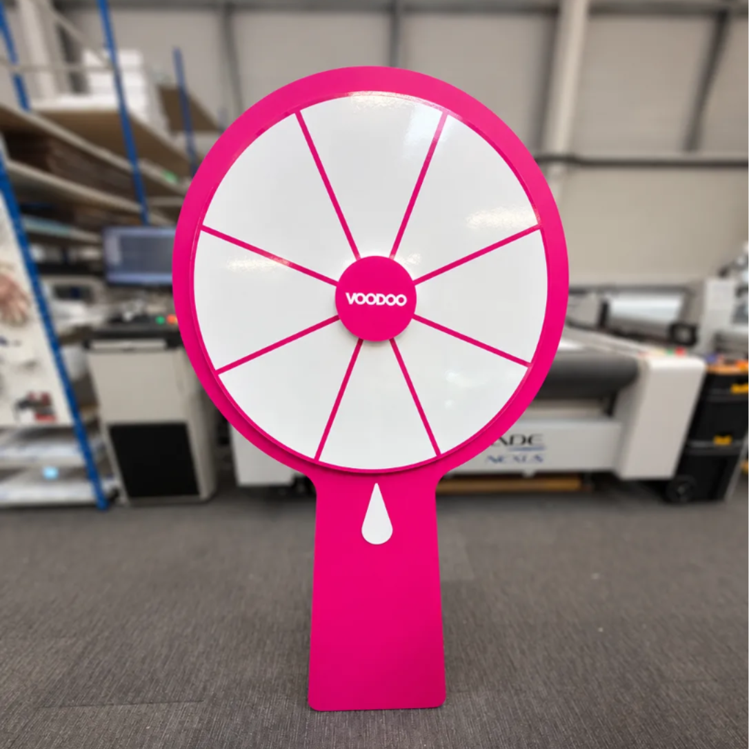 A large pink spinning wheel with the word "vooDoo" displayed on it, standing on a gray carpeted floor.