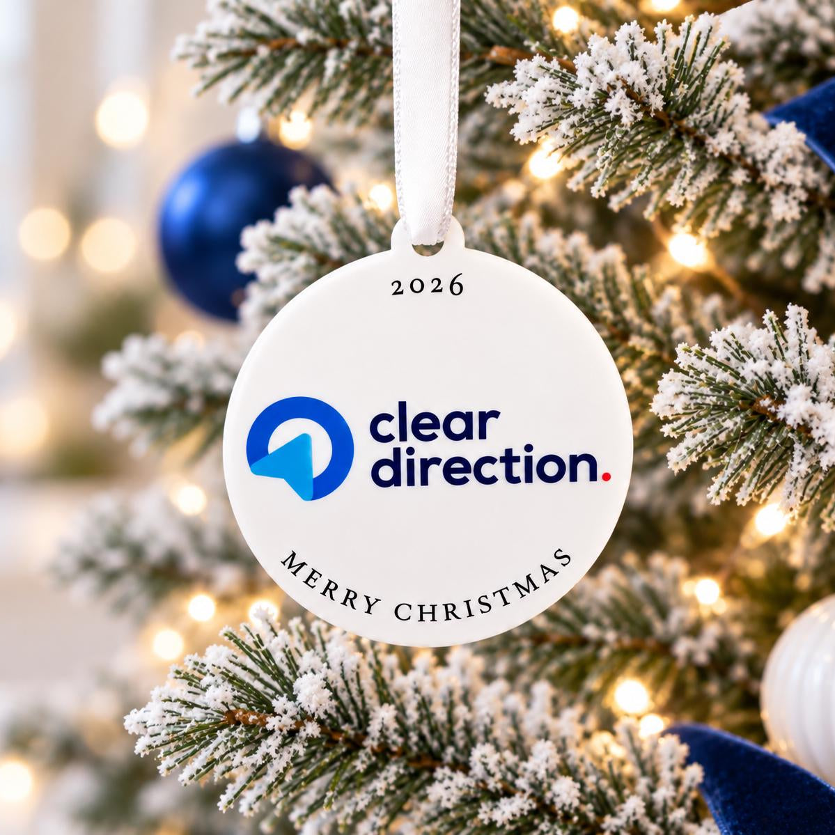 A white ornament with the text "cleardirection" and "Merry Christmas" hangs on a Christmas tree, surrounded by other ornaments and lights.