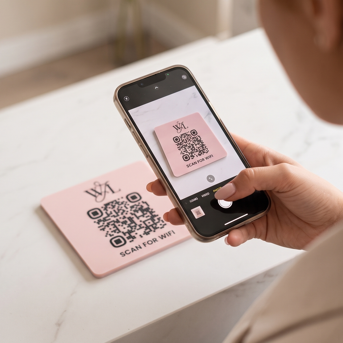 A person is holding a smartphone displaying a QR code on the screen, with a pink card featuring the same QR code in the background.