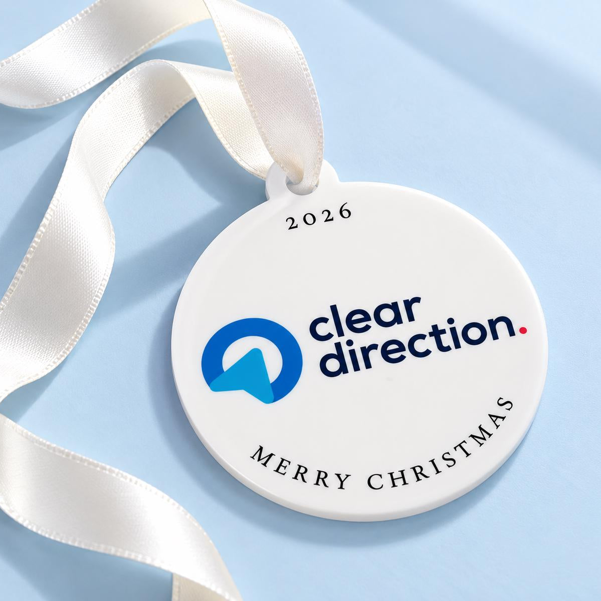 A white circular ornament with a ribbon, displaying the text "clear direction" and "MERRY CHRISTMAS" on it.