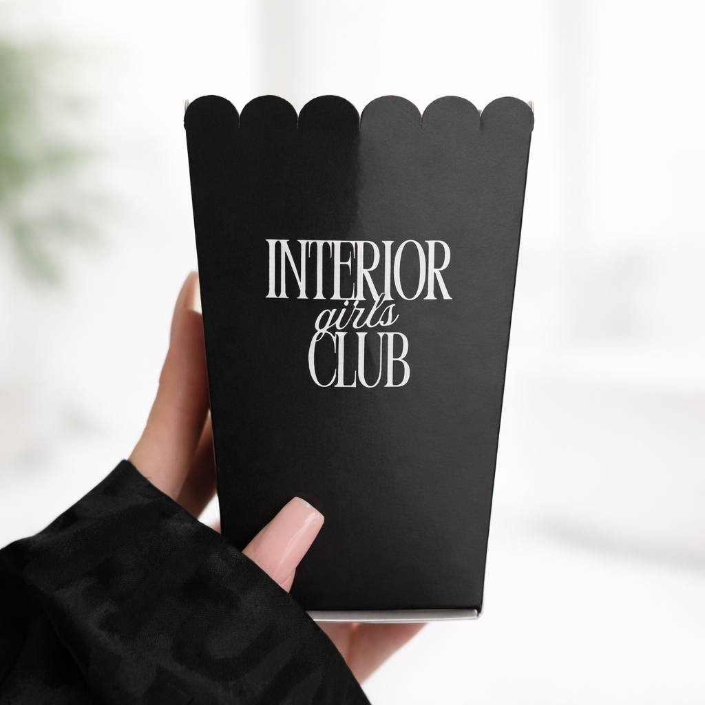 A hand holding a black container with the text "INTERIOR girls CLUB" printed on it.
