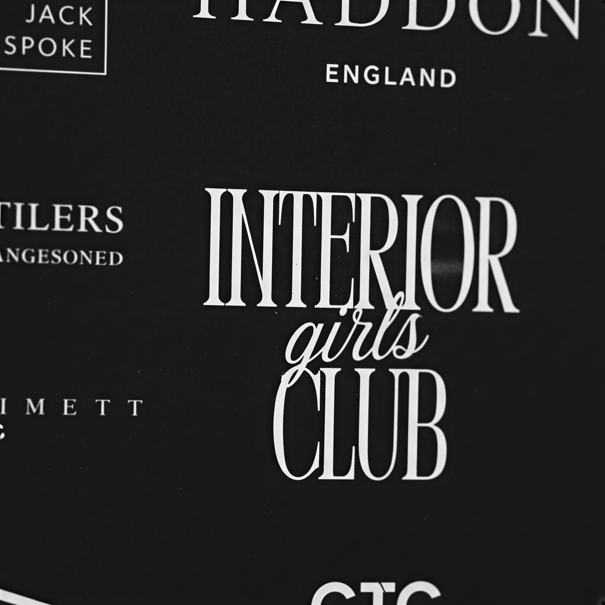 a close-up view of a black background with white text and logos. The text and logos appear to be related to a club or organization, but the exact content is not clear due to the close-up nature of the image.