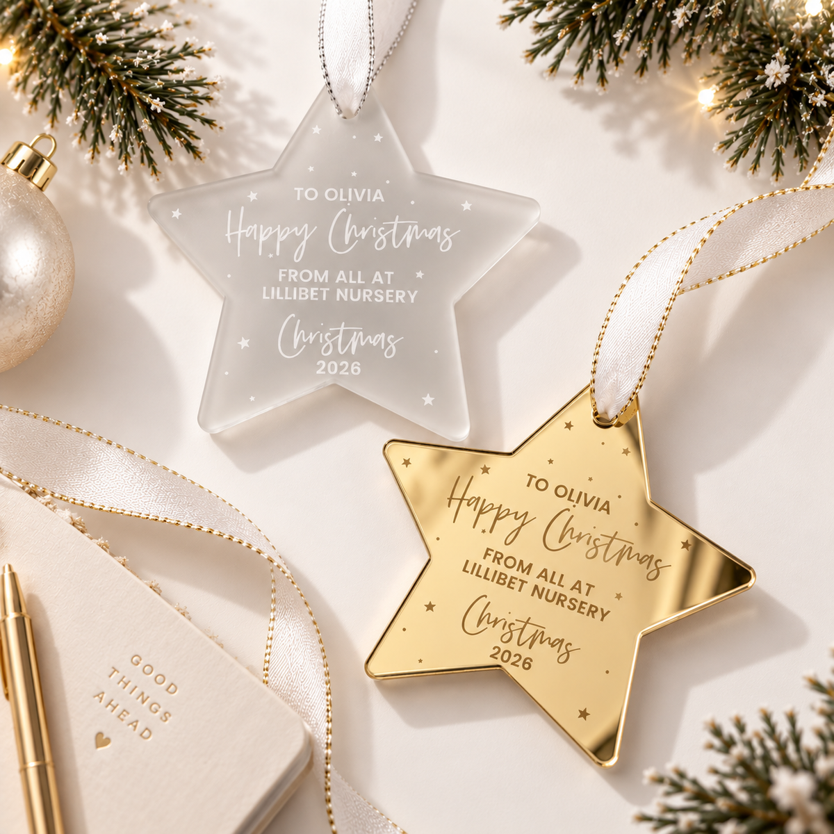 two star-shaped ornaments, one clear and one gold, hanging on a white background with greenery and a pen.