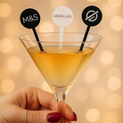 A hand holding a martini glass with cocktail stirrers, each with a different symbol on it.