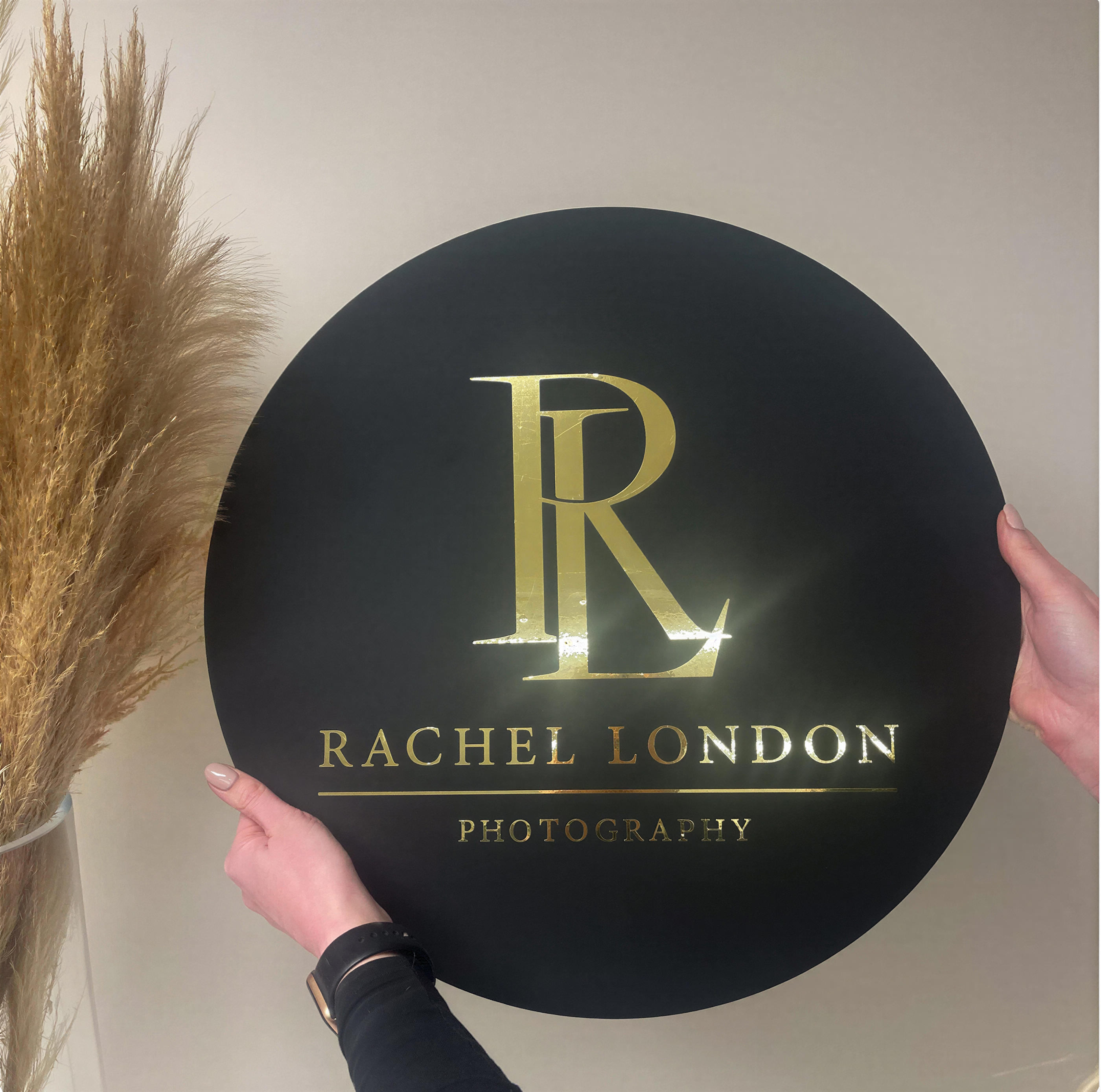 A person is holding a large black sign with the word "RACHEL LONDON" and "PHOTOGRAPHY" printed on it.
