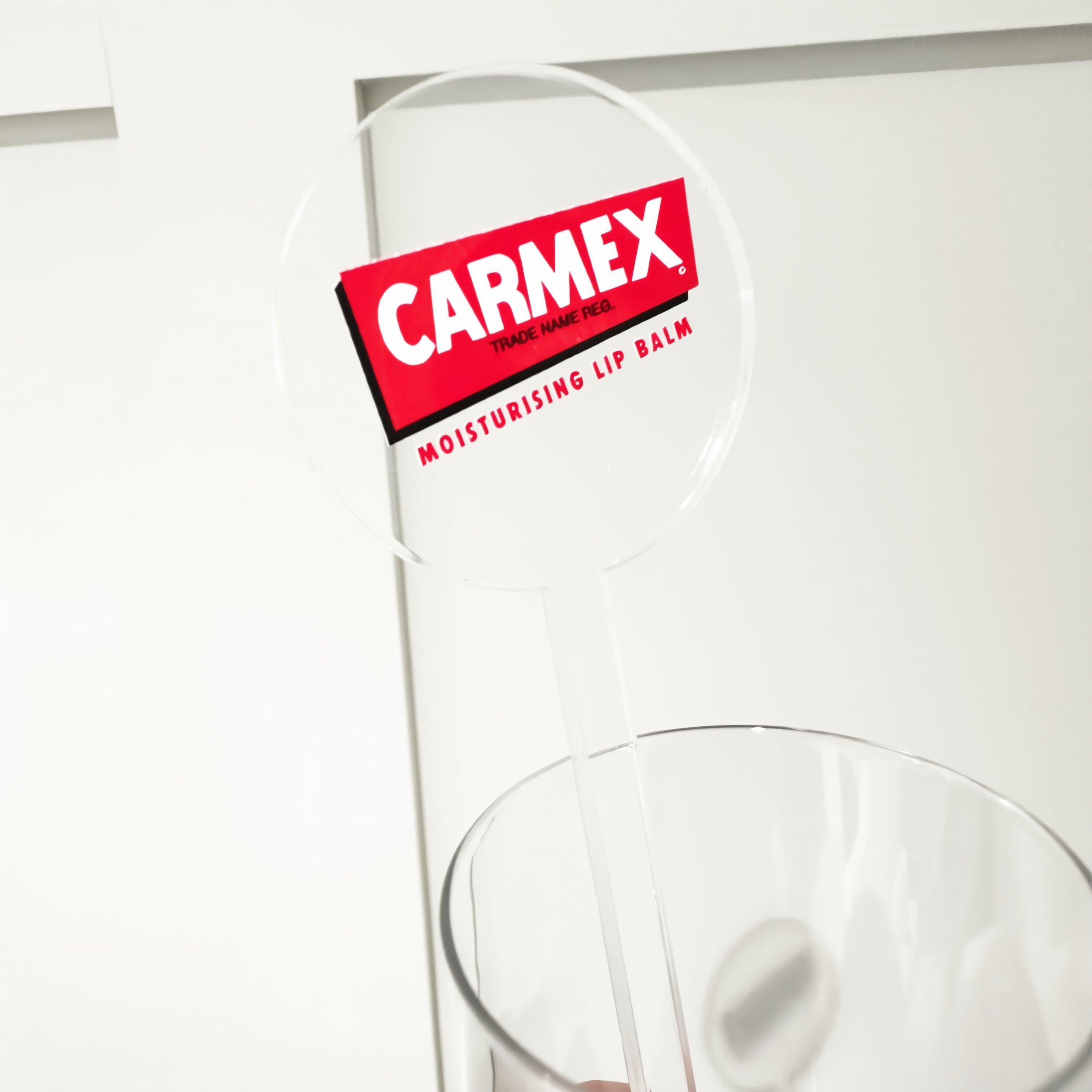 a clear plastic container with a red and white label that reads "CARMEX TRADE MARK REG. Moisturising LIP BALM".