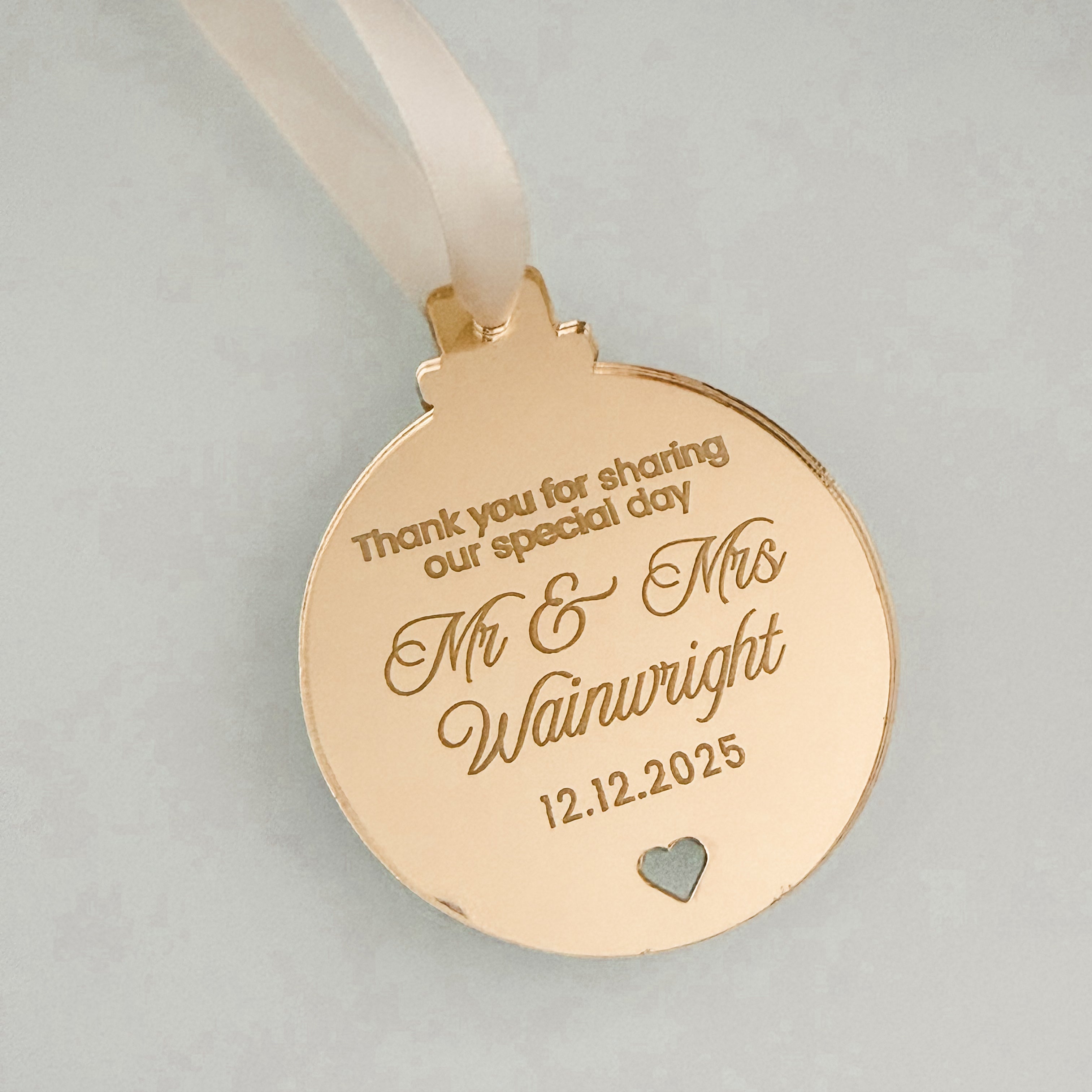 a pink ornament with a heart-shaped cutout, and it has a ribbon attached to it. The ornament has a message engraved on it, which reads "Thank you for sharing our special day Mr & Mrs 12.12.2025".