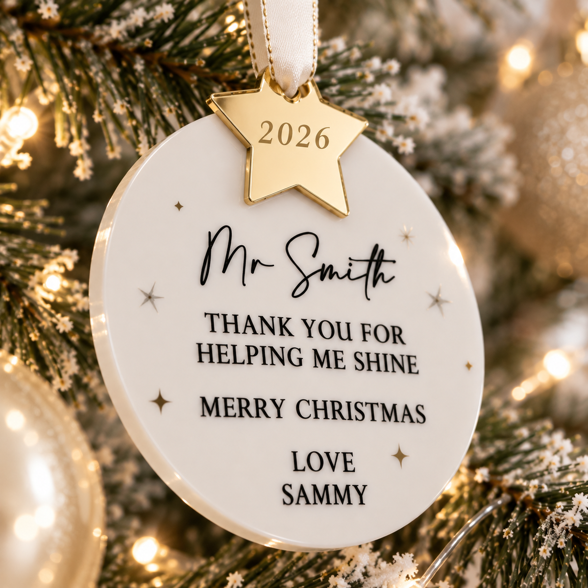 A white ornament with a gold star and the text "Mr. Smith" is hanging on a Christmas tree.