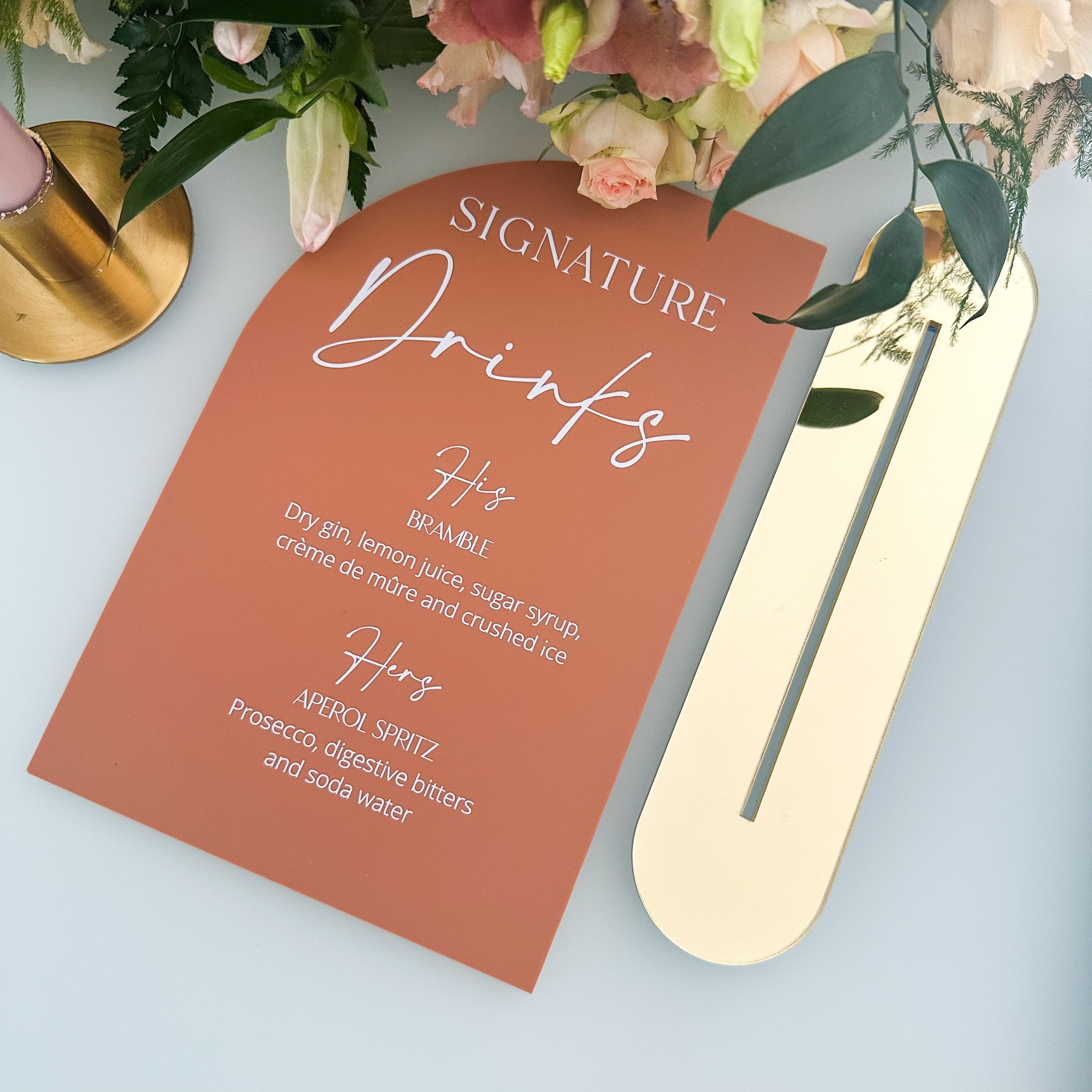 A collection of colorful name cards or place cards, each with a different color and text, placed on a white plate or napkin. The cards are arranged in a row, and there are flowers visible in the background.