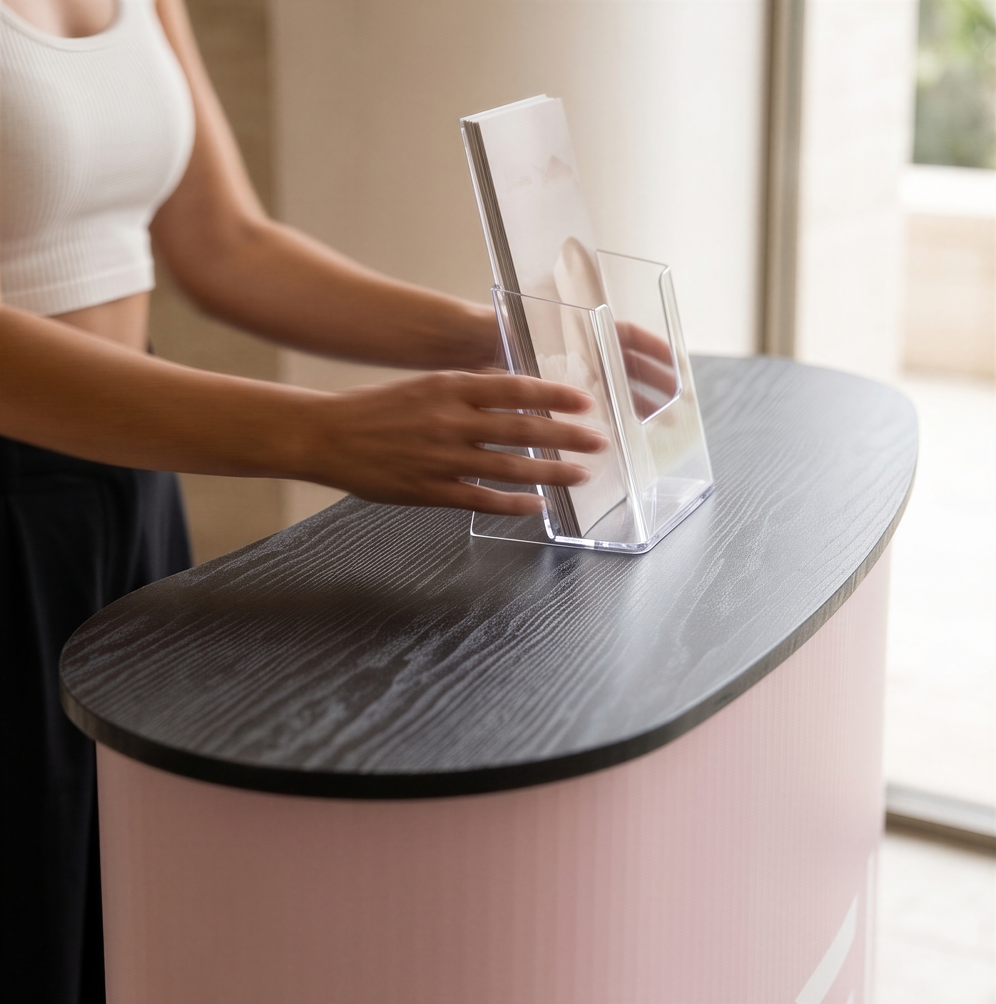 A person is standing behind a counter, holding a clear plastic tray with a magazine or brochure on it.
