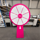 A large pink spinning wheel with the word "vooDoo" displayed on it, standing on a gray carpeted floor.