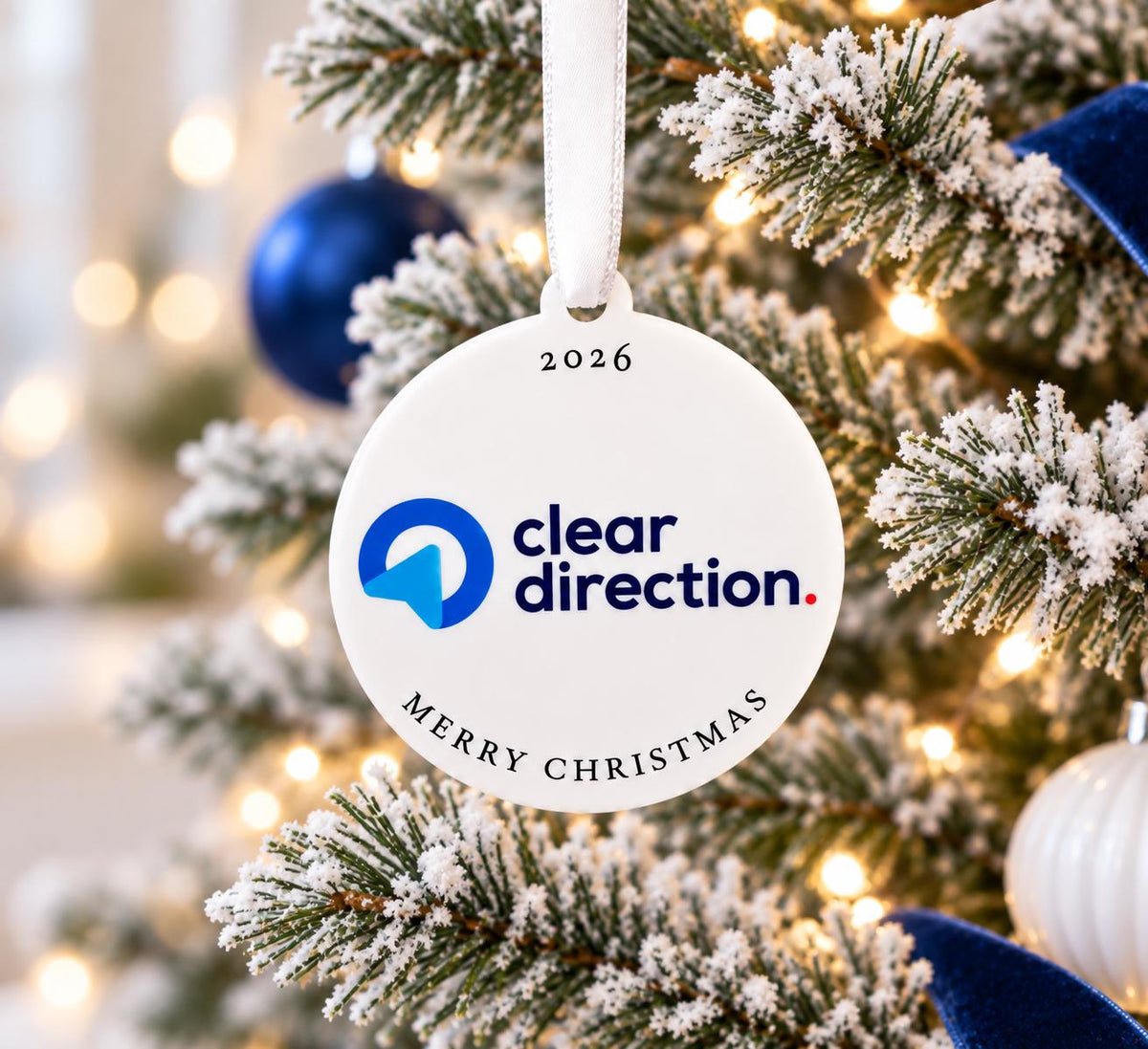 A white ornament with the text "cleardirection" and "Merry Christmas" hangs on a Christmas tree, surrounded by other ornaments and lights.