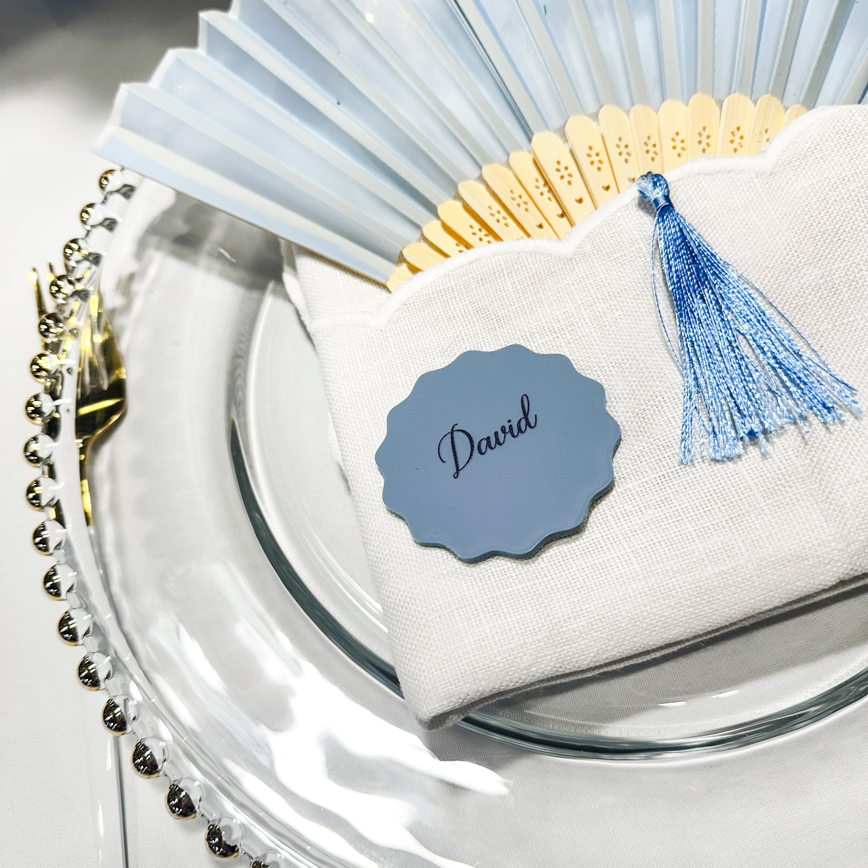 A collection of colorful name cards or place cards, each with a different color and text, placed on a white plate or napkin. The cards are arranged in a row, and there are flowers visible in the background.