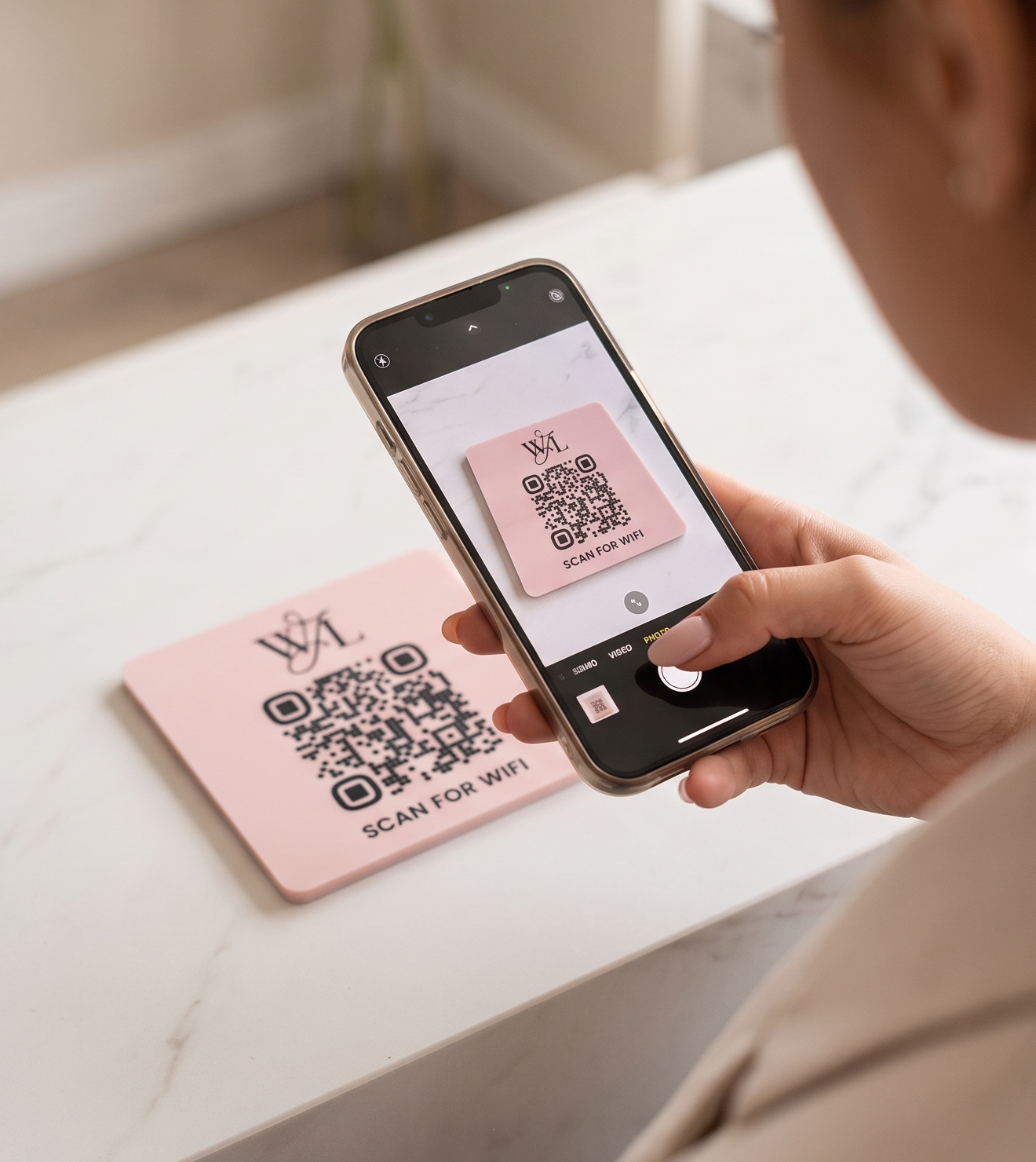 A person is holding a smartphone displaying a QR code on the screen, with a pink card featuring the same QR code in the background.