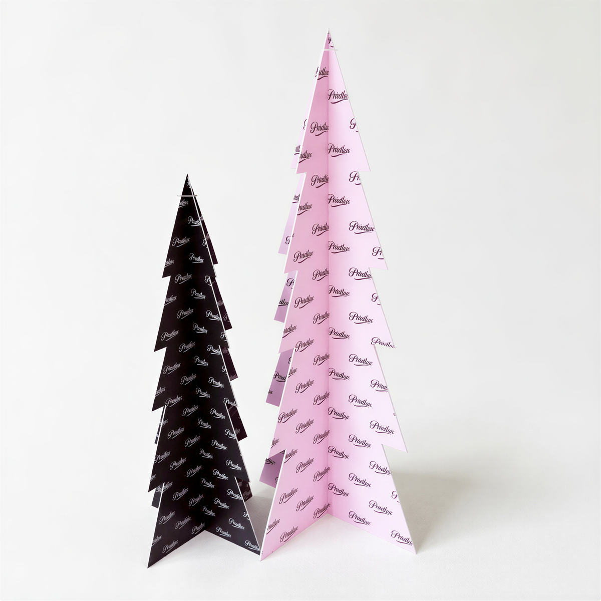 Two paper Christmas trees, one black and one pink, are standing side by side against a white background.