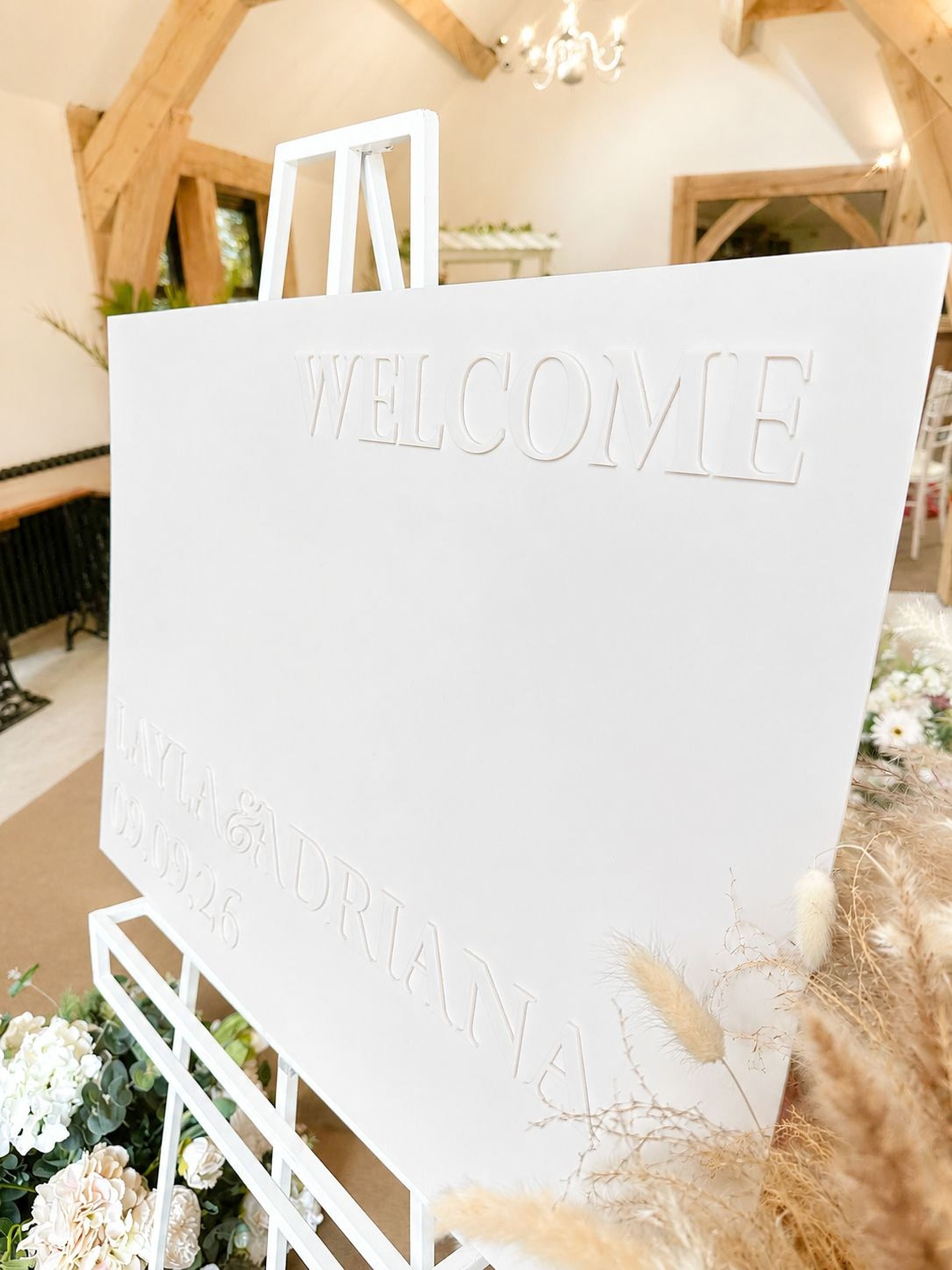 a white sign with the word "WELCOME" prominently displayed, along with the names "LAYLA & DRIANA" and the date "09.09.2026".