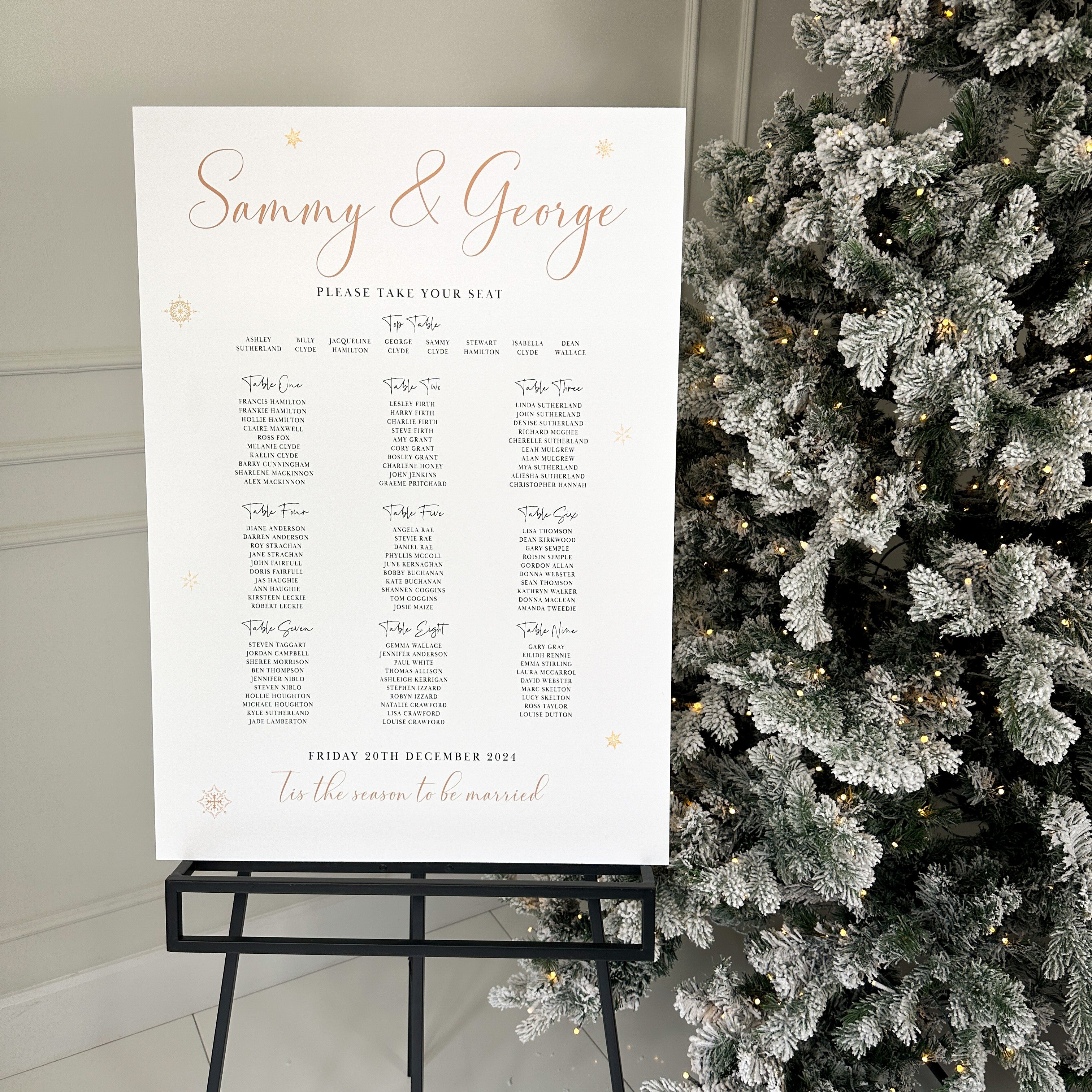 a wedding reception setup with a black and white colour scheme. There are two signs, one white and one black, both displaying the names of the couple, Sophie and Charlie. The white sign is positioned in front of the black sign, which is placed on a white stand. The stand also has a small floral arrangement on it.