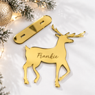 A golden deer-shaped ornament with the name "Frankie" engraved on it, placed on a white surface next to some Christmas lights and greenery.