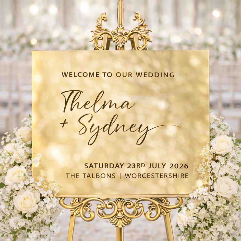 a wedding invitation sign with a gold frame and floral decorations.