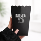 A hand holding a black container with the text "INTERIOR girls CLUB" printed on it.