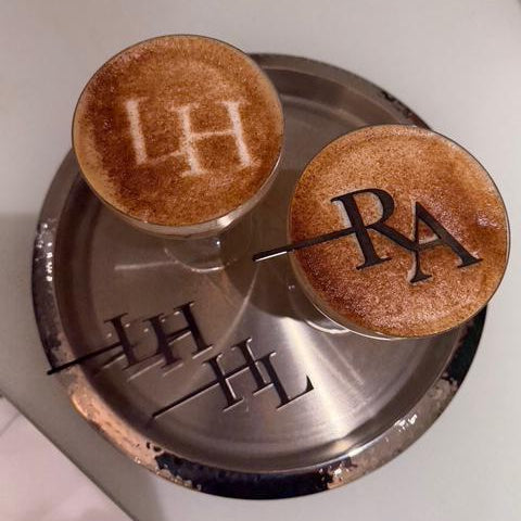 two coffee drinks with a logo on the foam, placed on a silver tray.