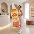A woman is holding a large cardboard cutout of a Rapunzel-branded bottle of hair syrup in a store.